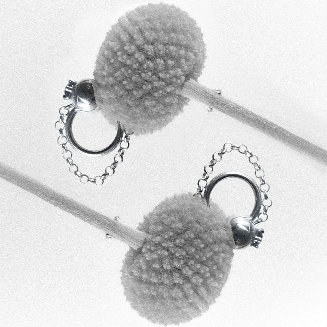 two ear cuffs with chains, sphere and gemstone on a flower light grey background