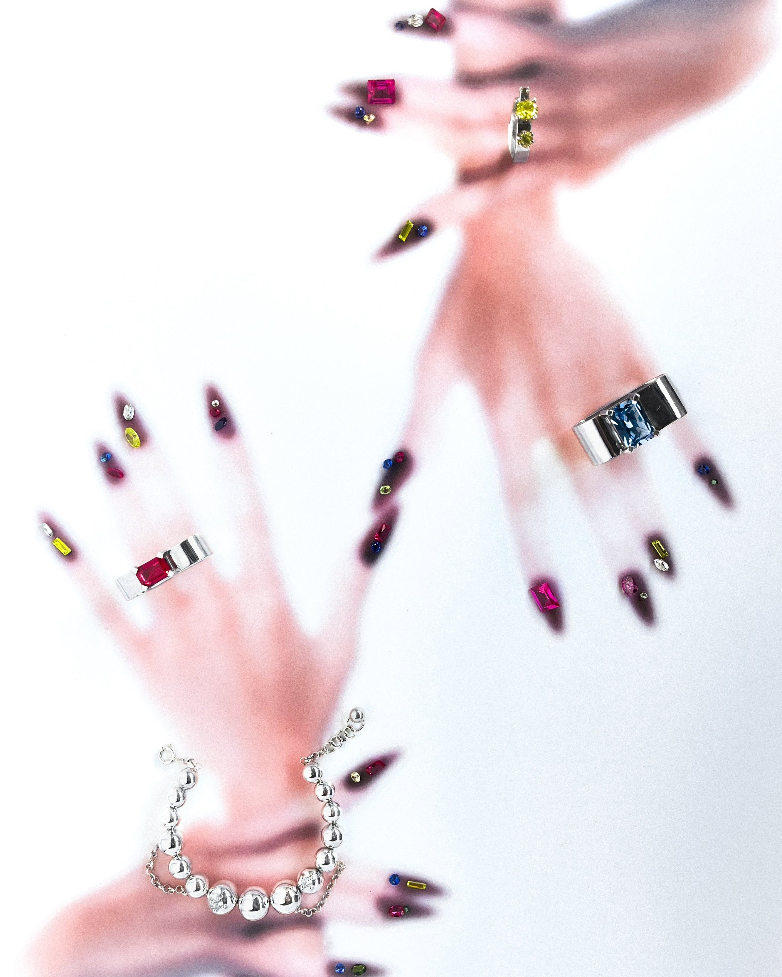 Close-up of hands with colorful nail polish wearing various pieces of jewelry on a white background