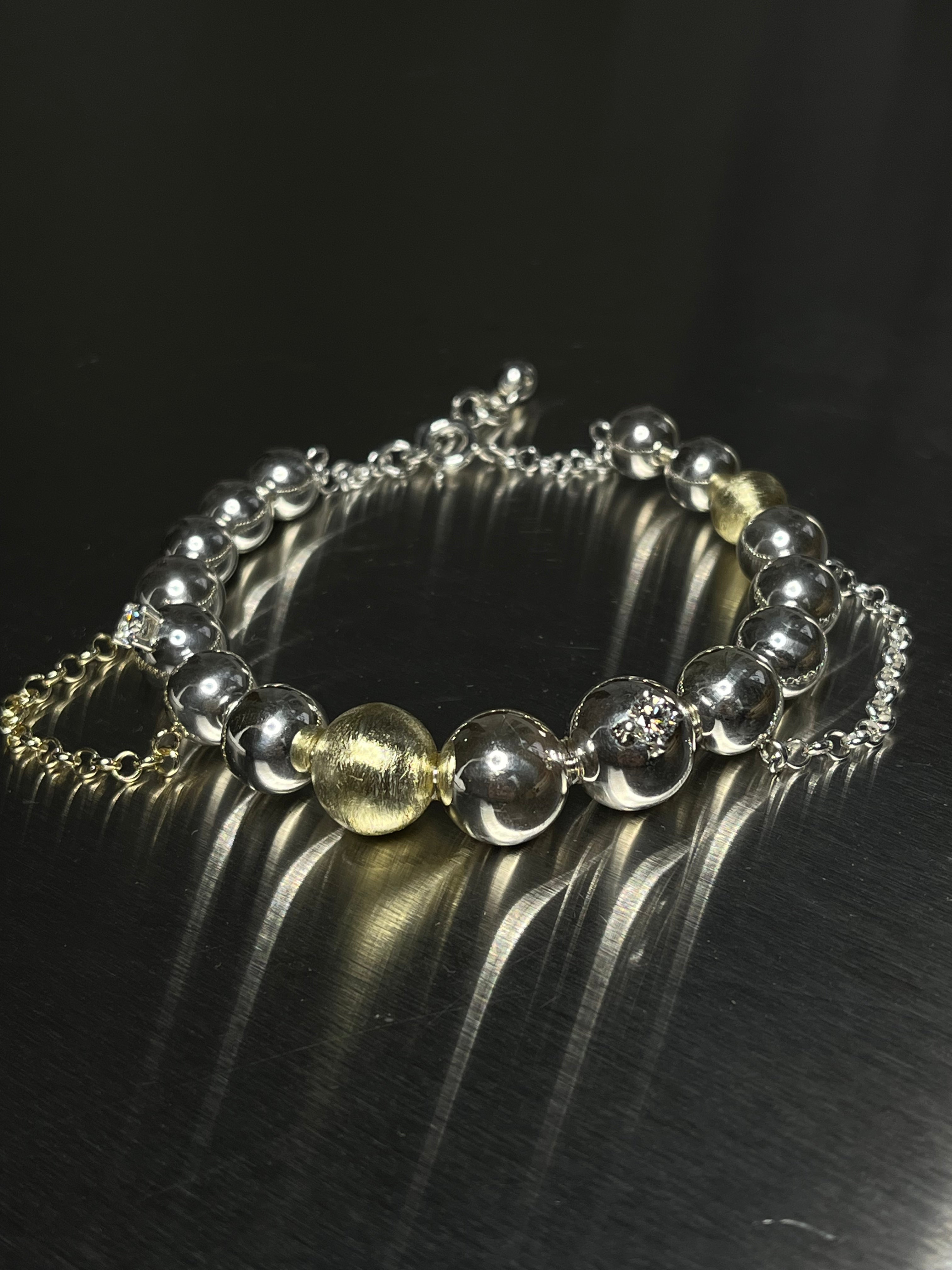 Bracelet with silver, gold, chains and two diamonds on a dark surface