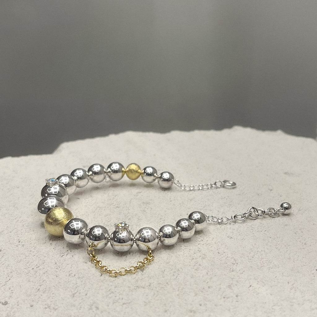 Bracelet with silver and gold beads, chains and two diamonds on a textured surface