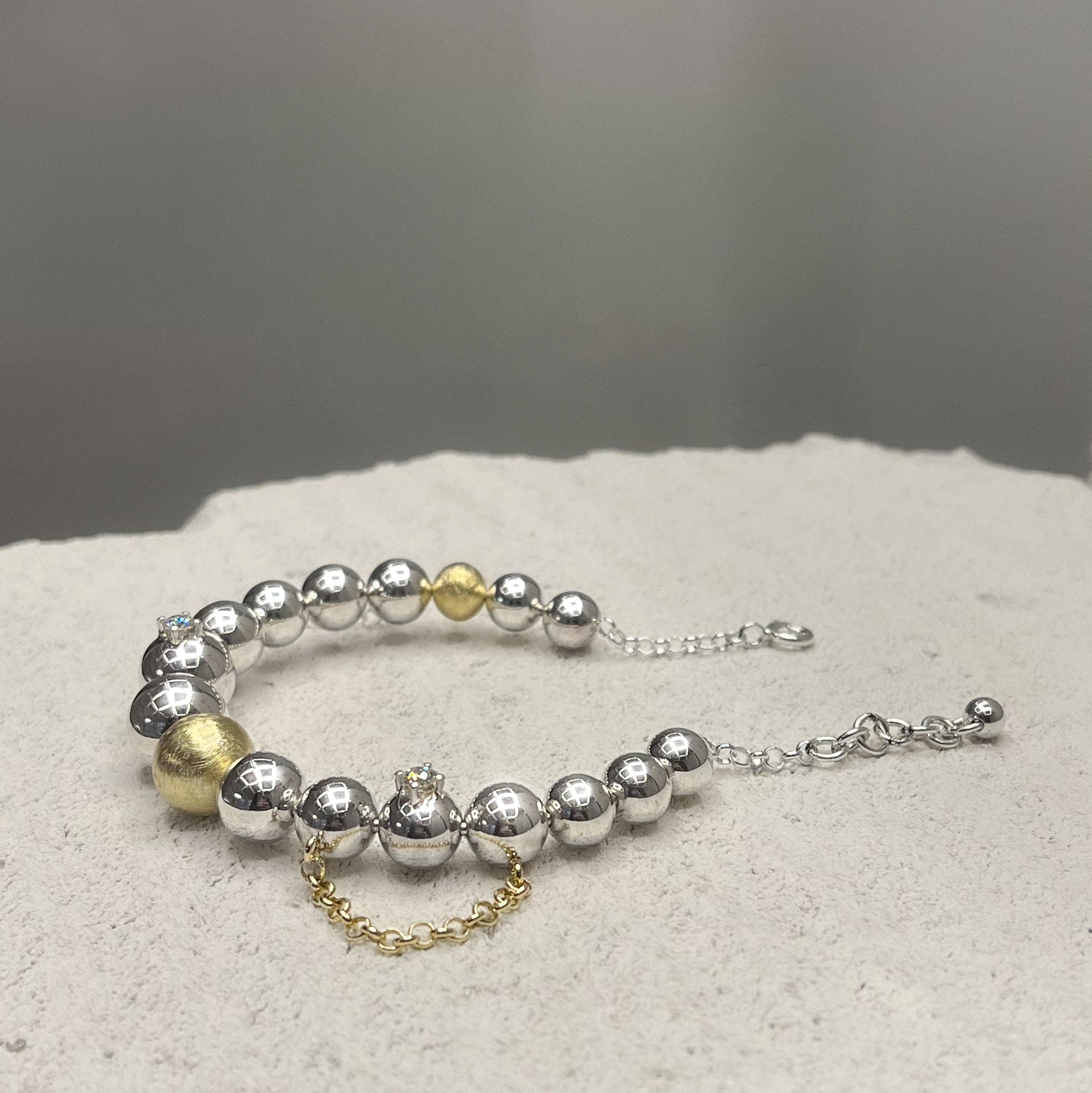Bracelet with silver and gold beads, chains and two diamonds on a textured surface