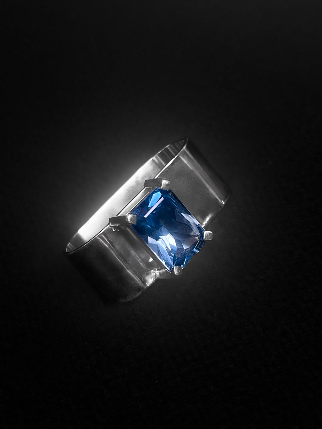 Silver statement monumental brutalistic  ring with a blue topaz gemstone on a black background