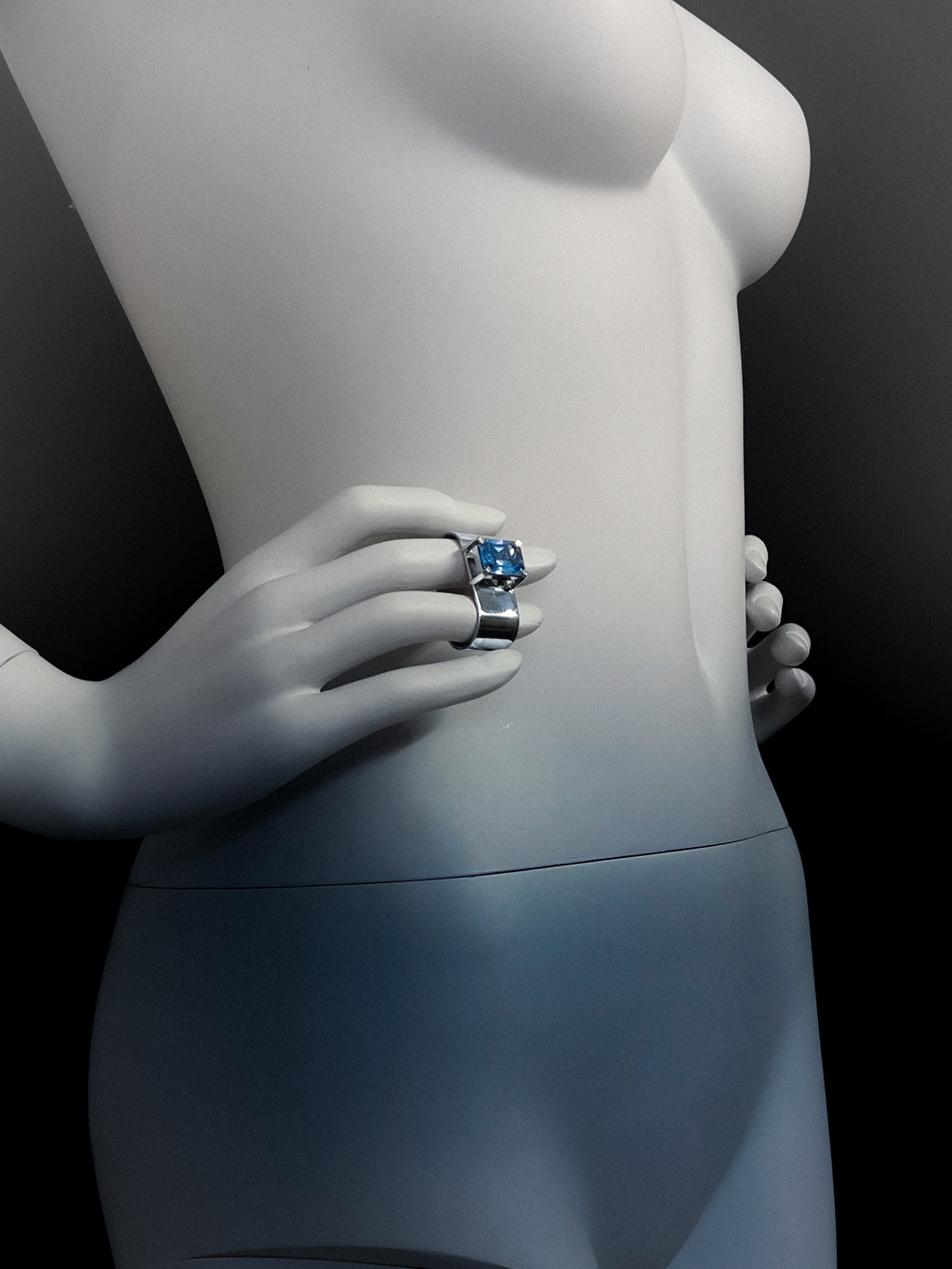 Mannequin wearing a monumental brutalistic ring with a blue topaz gemstone on a black background