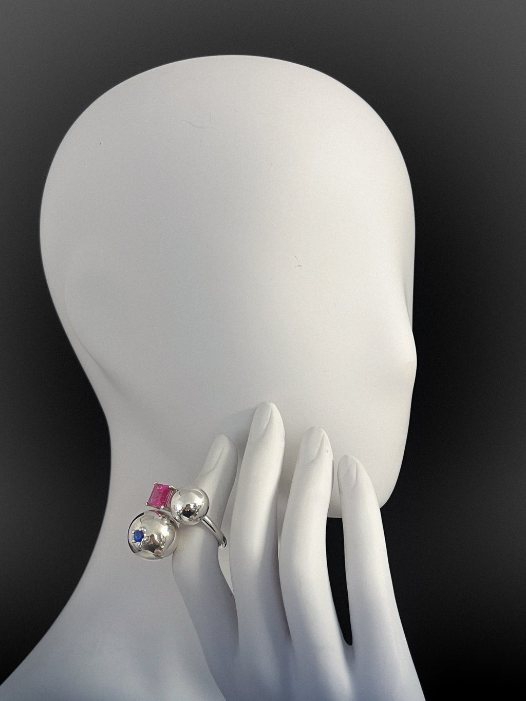 Silver ring with colorful stones on a white mannequin hand against a black background