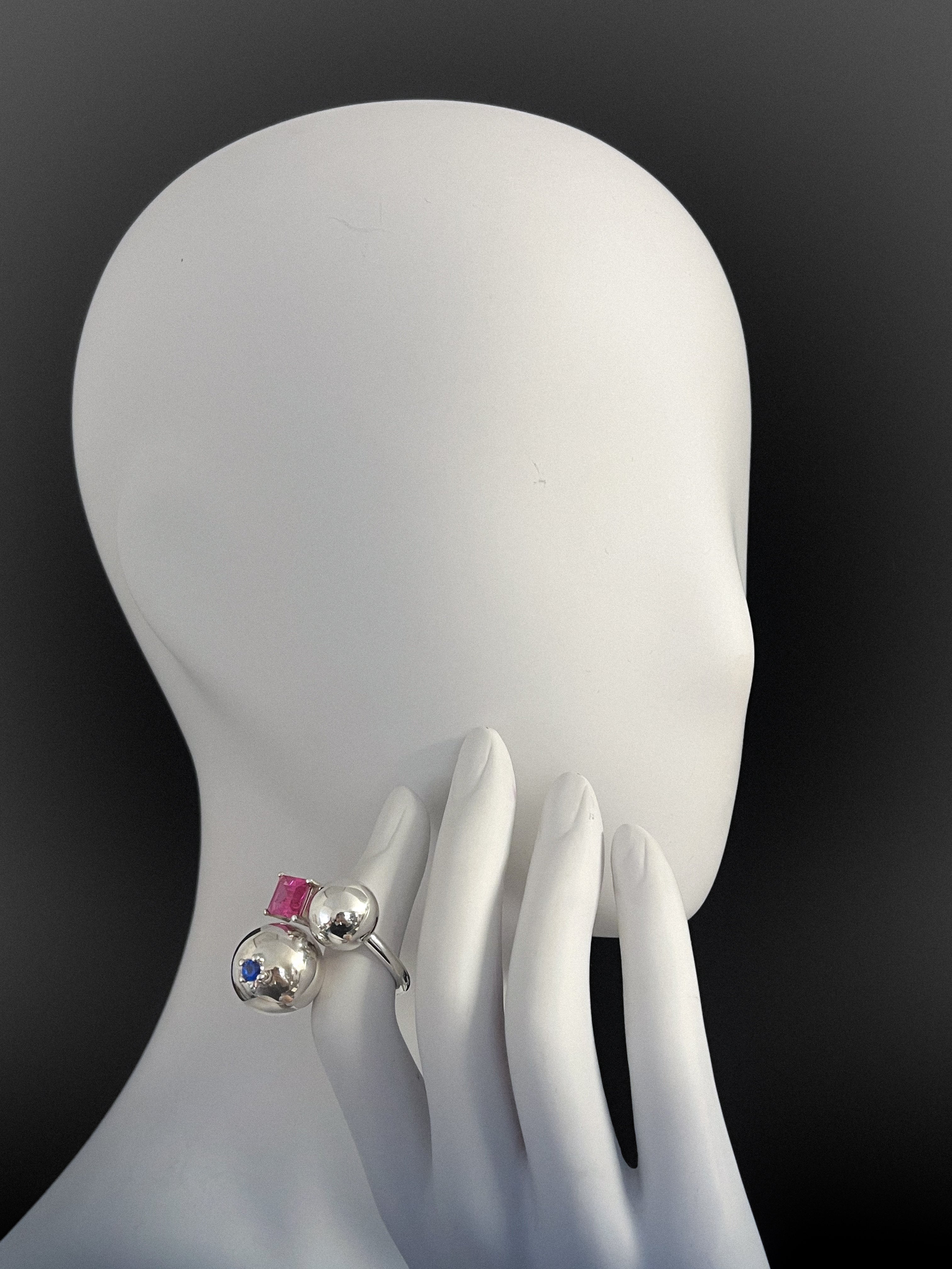 Silver ring with colorful stones on a white mannequin hand against a black background
