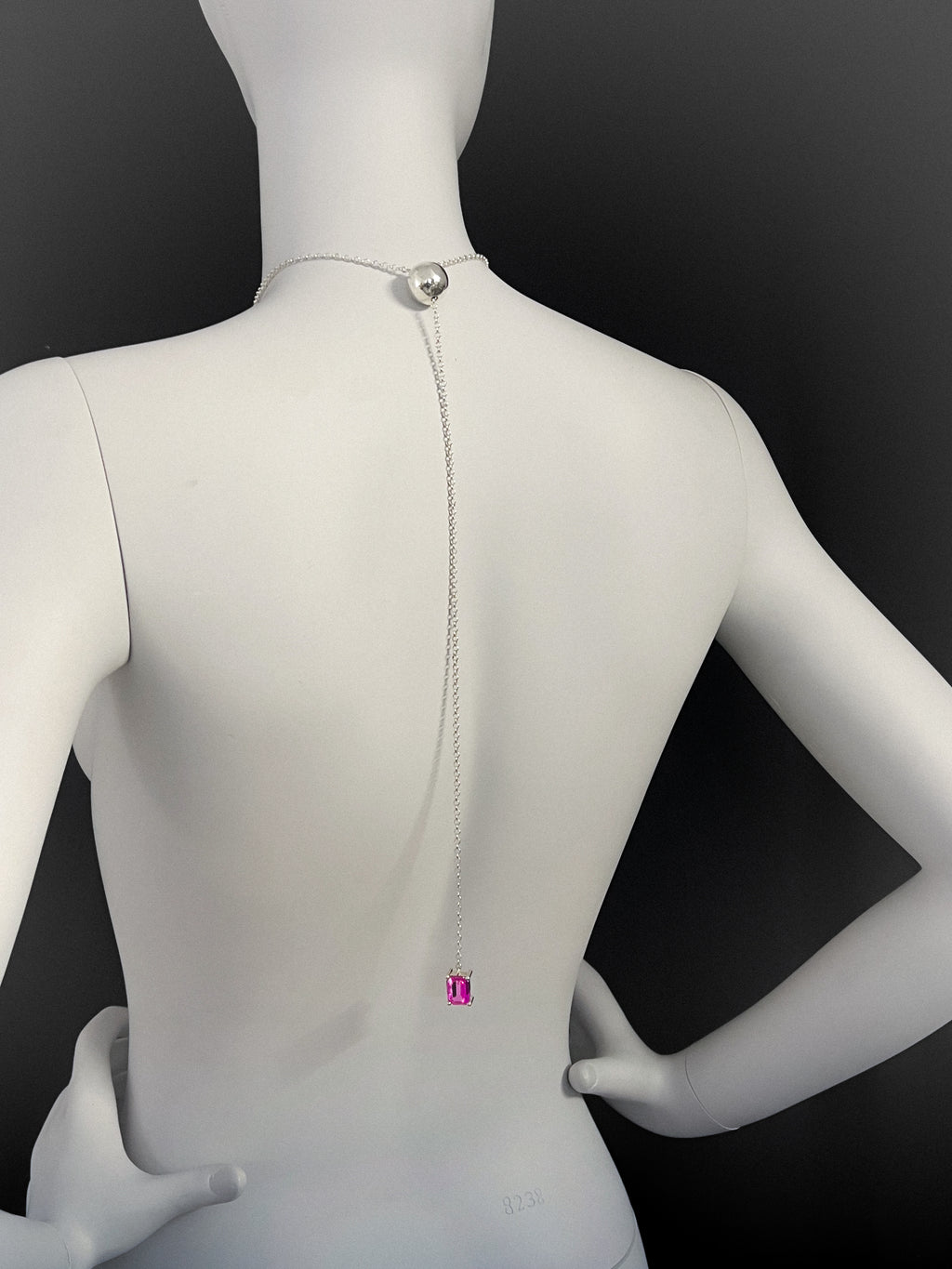 Mannequin wearing a long adjustable necklace with a sphere and pink gemstone on a black background