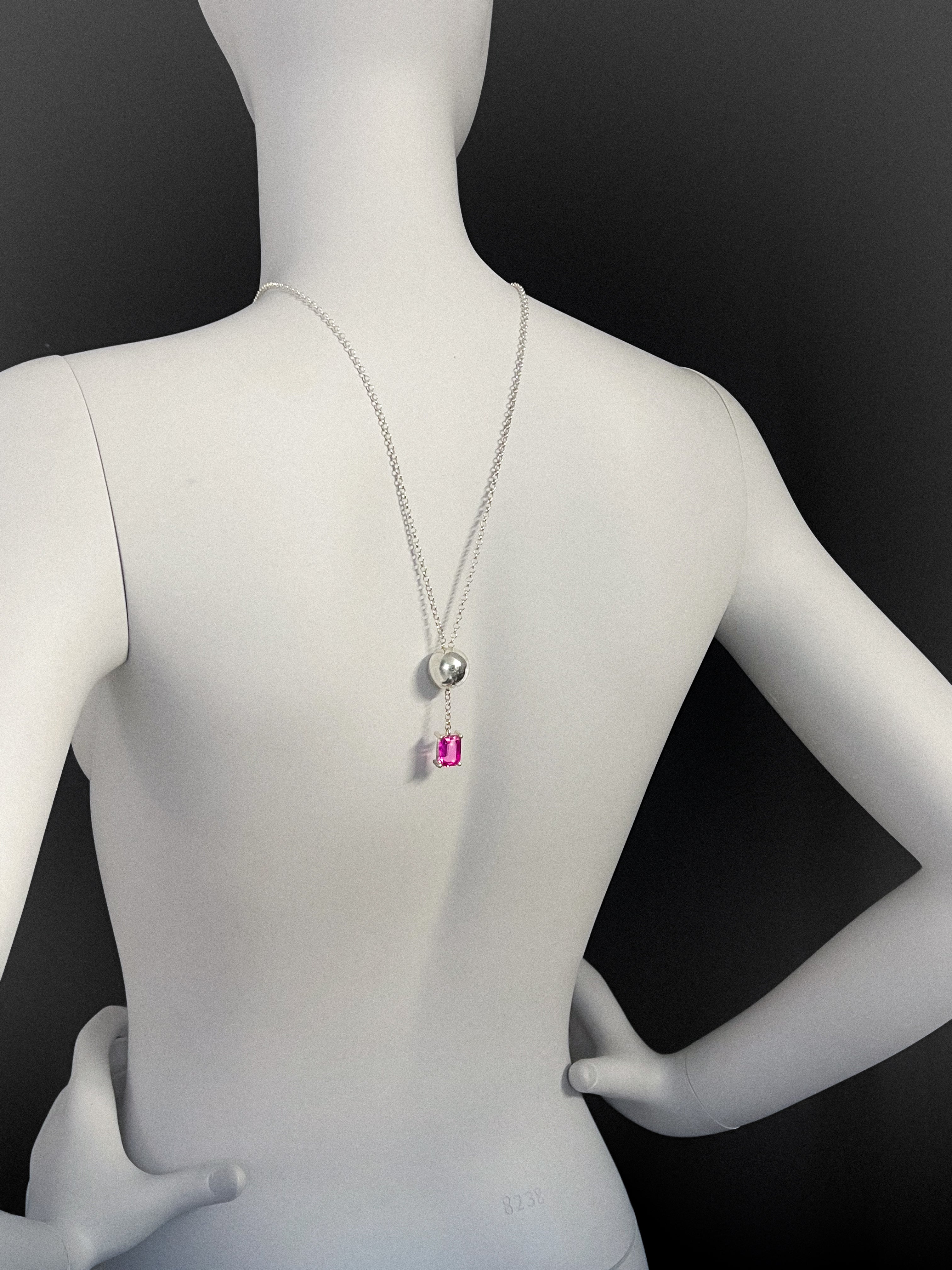 Mannequin wearing a long adjustable necklace with a sphere and pink gemstone on a black background