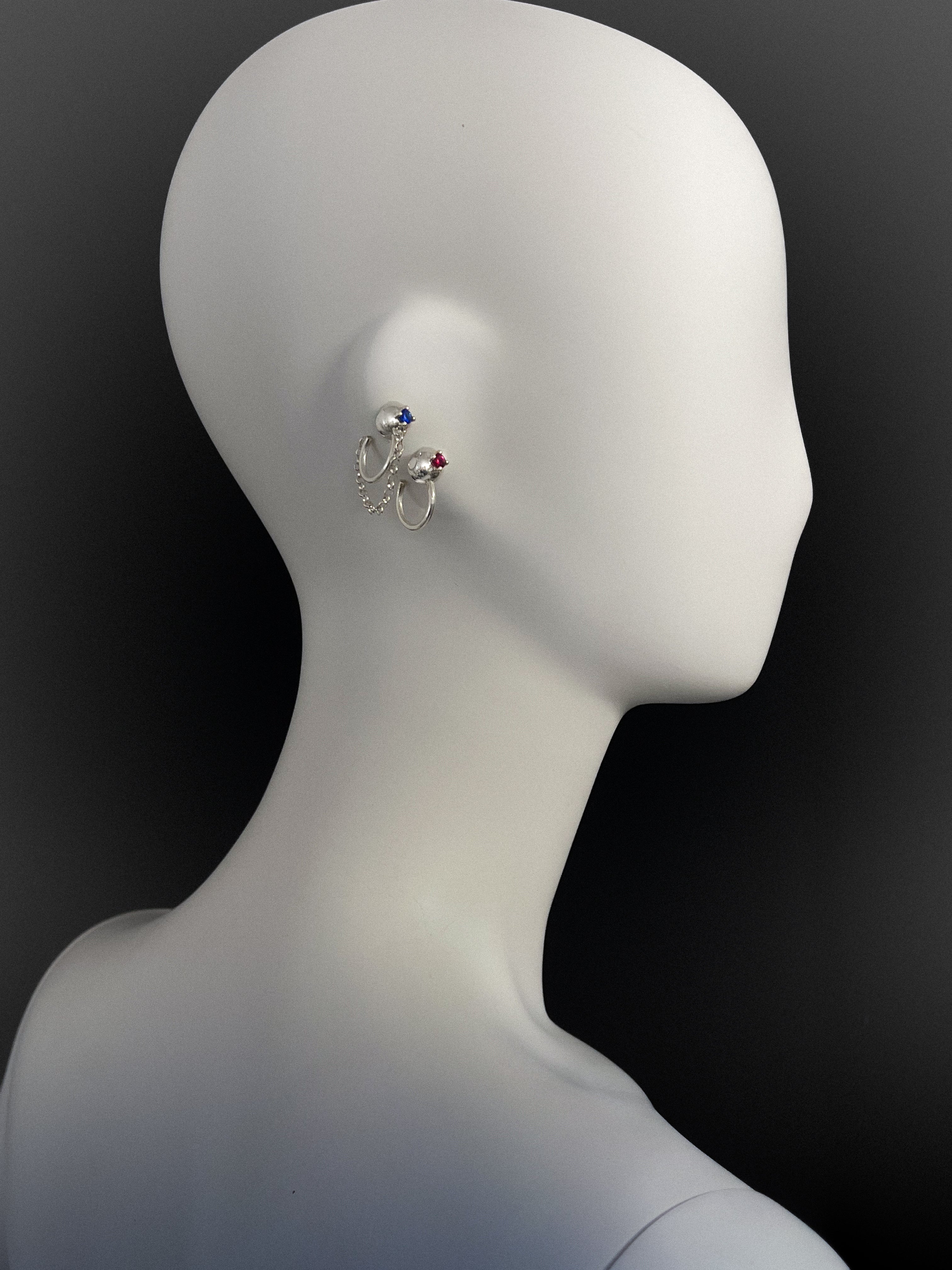 Silver ear cuffs with colored stones on a mannequin head against a black background