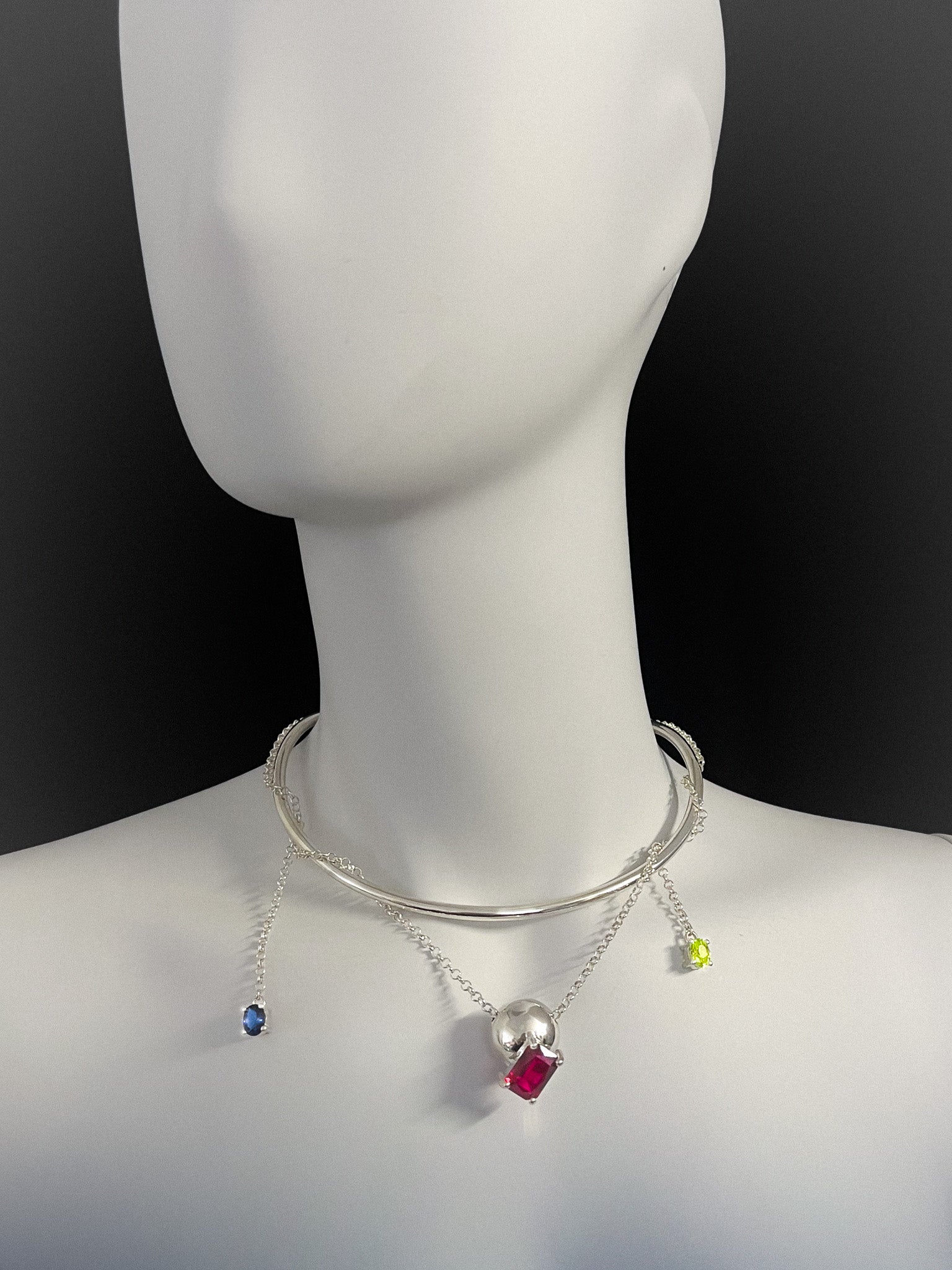 Mannequin wearing a silver choker necklace with chains, colorful gemstones on a black background