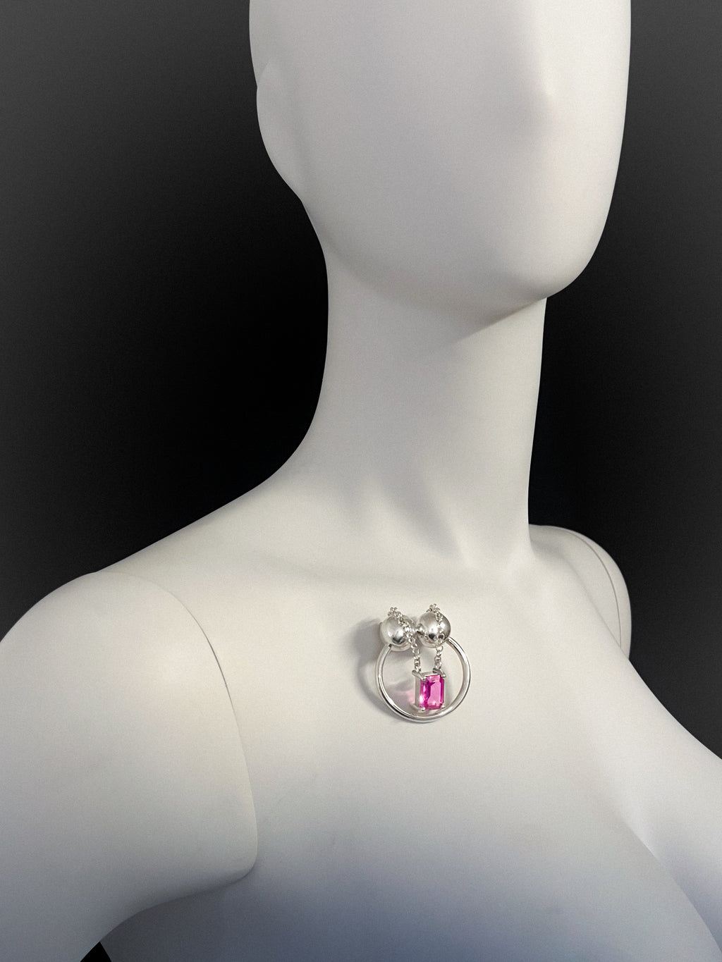 Mannequin wearing a silver brooch with a pink gemstone on a black background